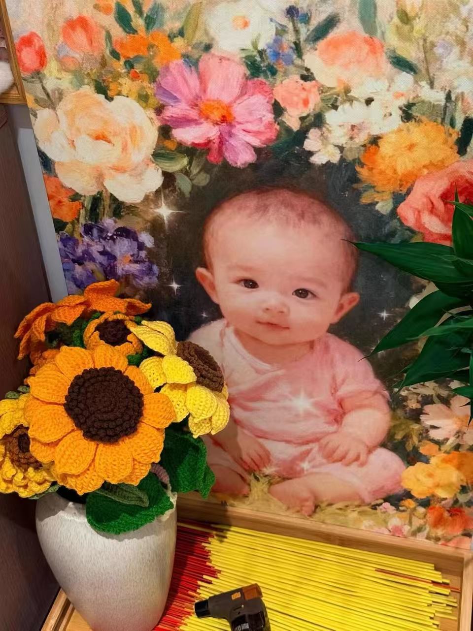 家中一角：孩子的画像被画成花丛中的样子，画前摆着一瓶手工钩织的向日葵和一盆绿植，下方是一排立着的香